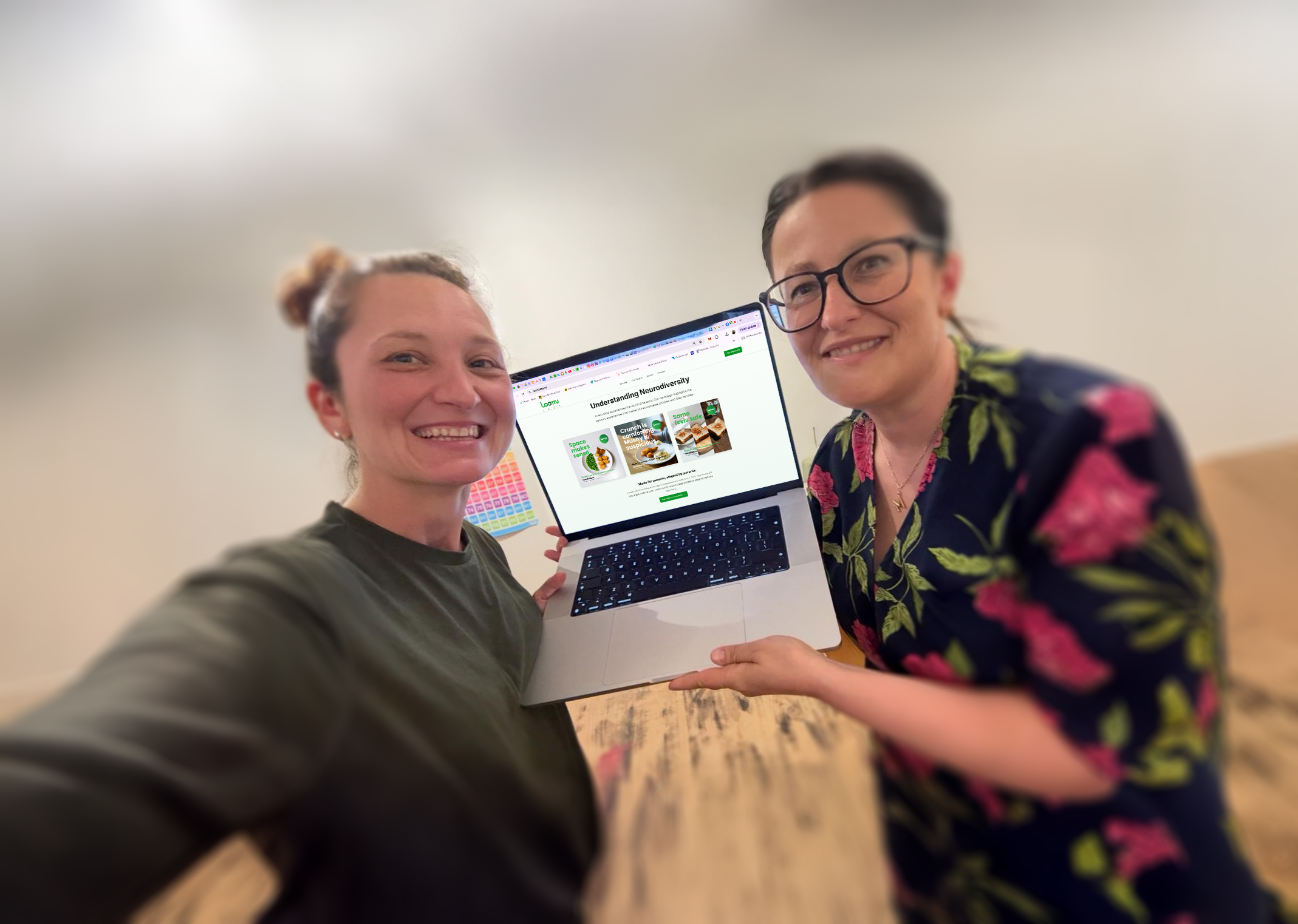 Aga and Kasia, the founders of Loomi Labs, smiling and holding a laptop showing the Loomi Labs website